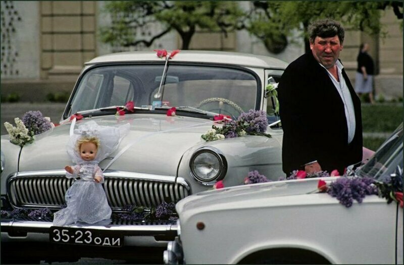 Водитель со своей машиной, украшенной свадебными цветами и куклой, ждет жениха и невесту после их свадьбы.