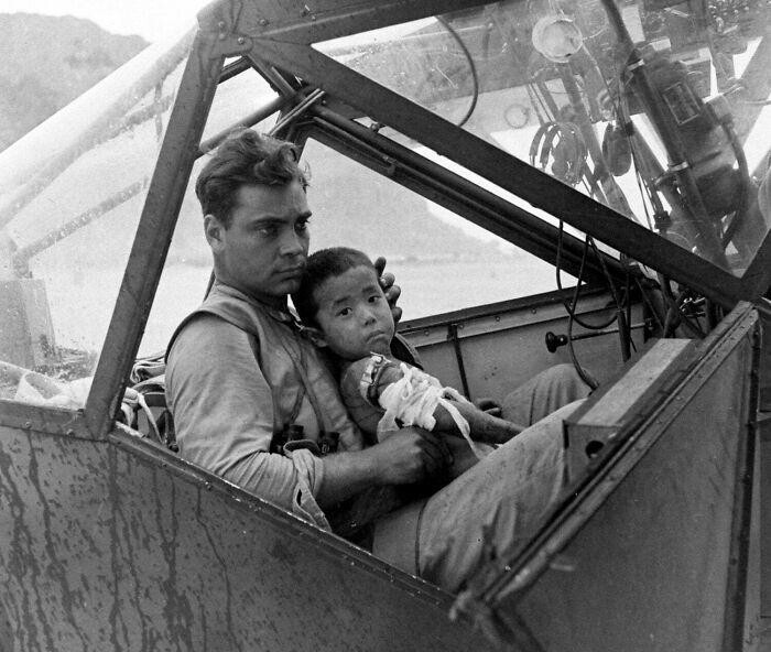 Американский солдат укрывает от дождя раненого японского мальчика в кабине самолета во время битвы за Сайпан, ожидая его транспортировки в полевой госпиталь. Июль 1944 года