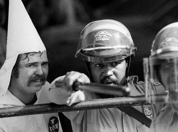 Член Ку-клукс-клана укрывается за чернокожим полицейским, после того, как толпа протестующих окружила собрание клана в Остине, Техасе. 1983 год