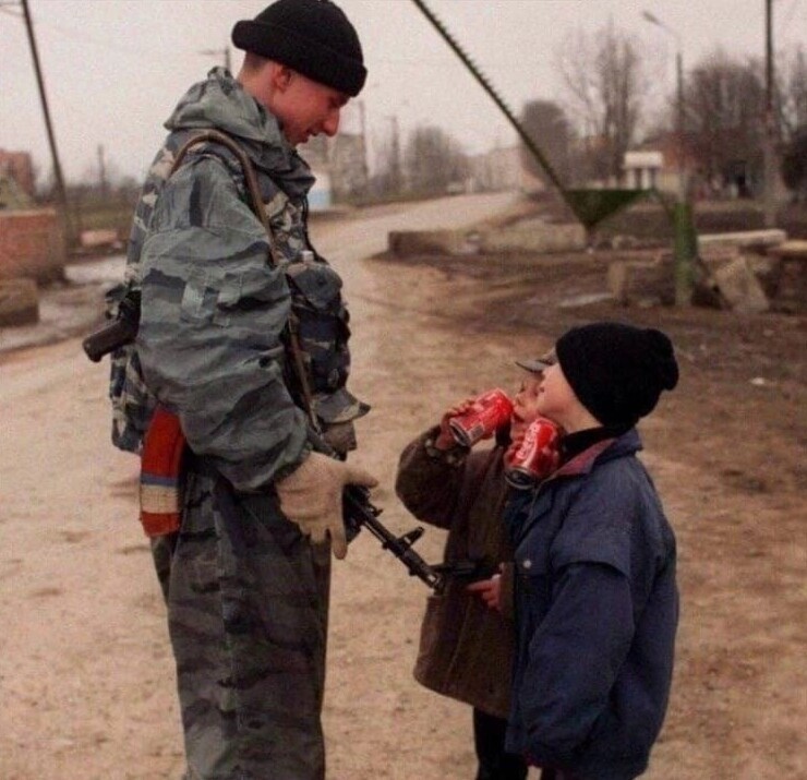 Солдат федеральных сил угощает чеченских ребят кока-колой. 1996 год