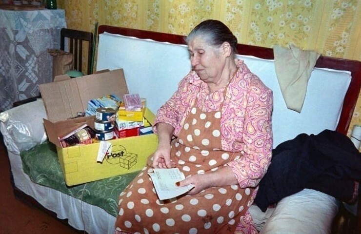 Пожилая женщина открывает коробку с продуктами и лекарствами из гуманитарной помощи, полученной от немецких организаций. Продовольственный кризис в России. 1990-е