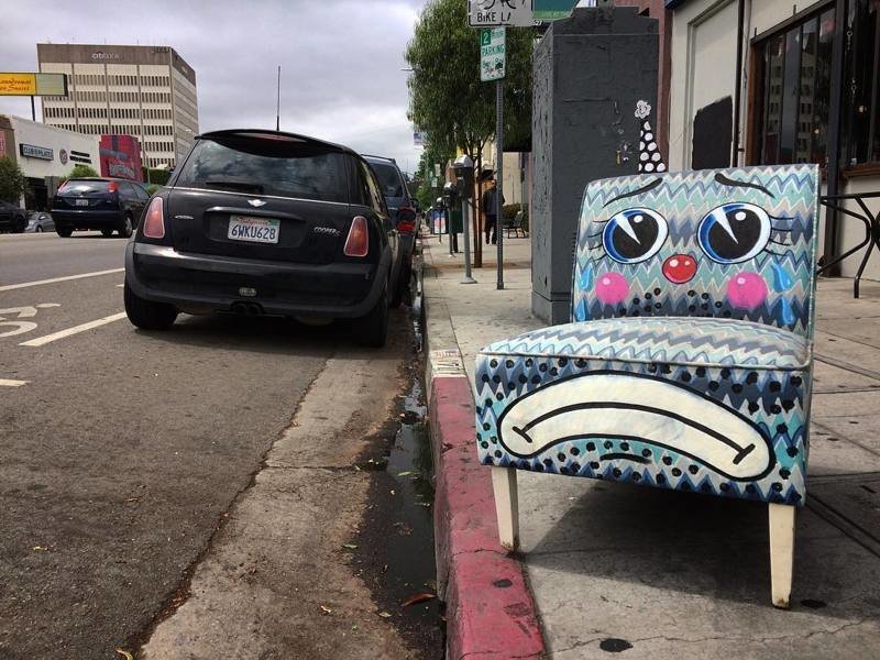 Художник  рисует рожицы грустных клоунов на выброшенных креслах и диванах